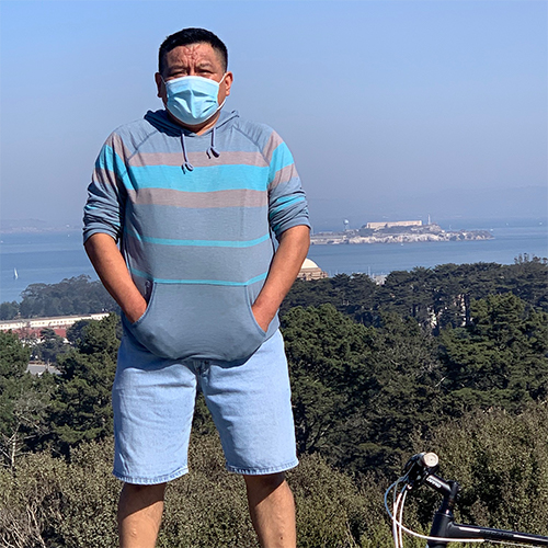 Man with striped long sleeve standing with Bay and Alcatraz Island in background