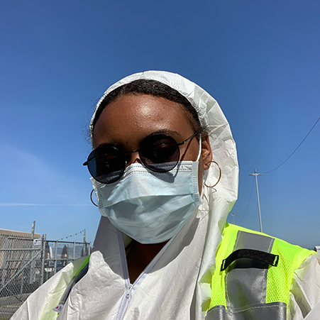 woman in personal protective gear (suit and mask) wearing sunglasses and hoop earrings