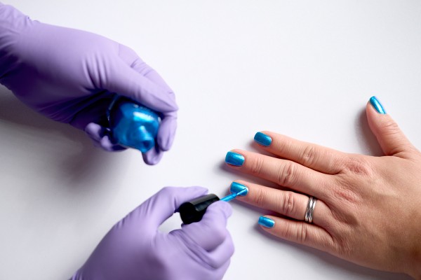 Two gloved hands applying blue nail polish on another set of hands. 